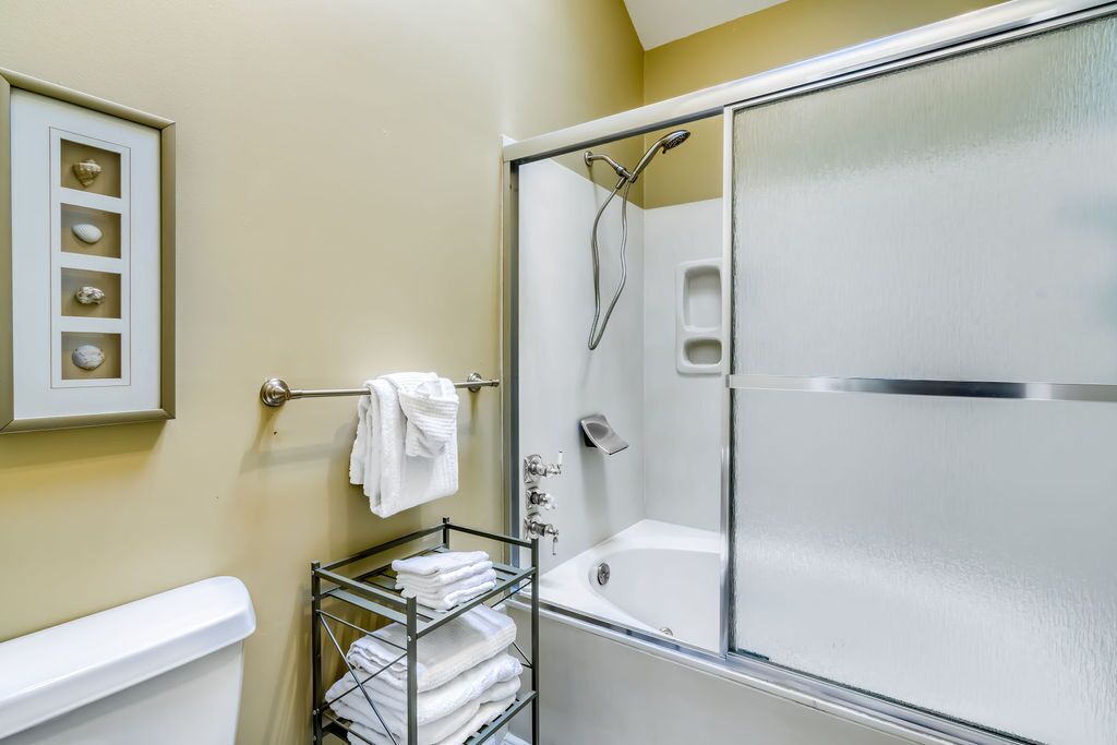 Un baño con ducha de mampara de vidrio, bañera blanca y toallero con toallas dobladas.