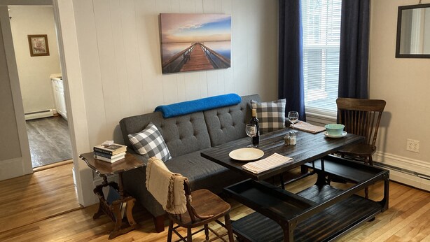 Ein Wohnzimmer mit grauem Sofa, einem Couchtisch und einem Gemälde eines Piers an der Wand.