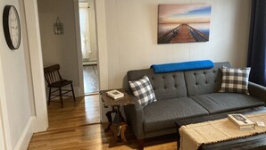 Ein Wohnzimmer mit grauem Sofa, einem Holztisch und einem Bild eines Piers an der Wand.