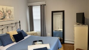 Ein Schlafzimmer mit Bett, Kommode, Fernseher und einem Fenster mit Vorhängen.