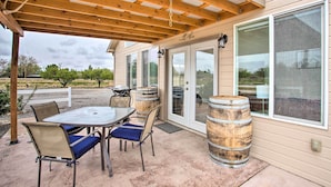 Eine überdachte Terrasse mit Tisch und Stühlen, Holzfässern und einem großen Fenster.
