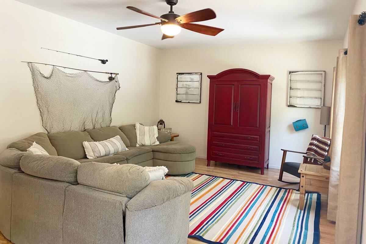 A living room with a sectional sofa, a red wardrobe, a ceiling fan, and a colorful striped rug.