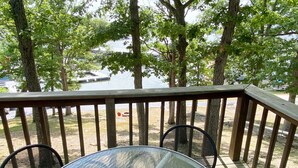 A wooden deck with a glass table and two chairs, overlooking a body of water and trees. - Niangua Hills Resort (Camdenton)