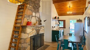 A kitchen with a stone fireplace, wooden ceiling, and a dining area with green chairs. - Niangua Hills Resort (Camdenton)
