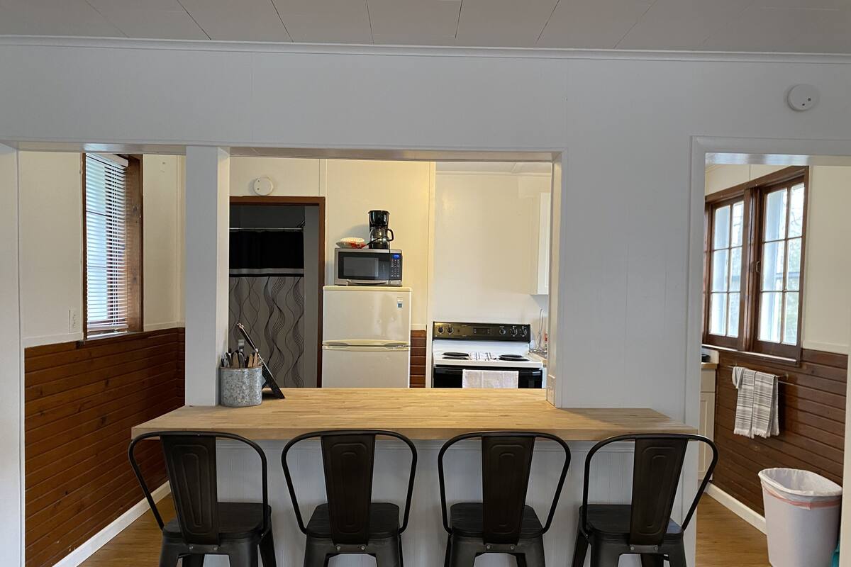 A kitchen with a wooden island, four bar stools, a microwave, a stove, and a sink.
