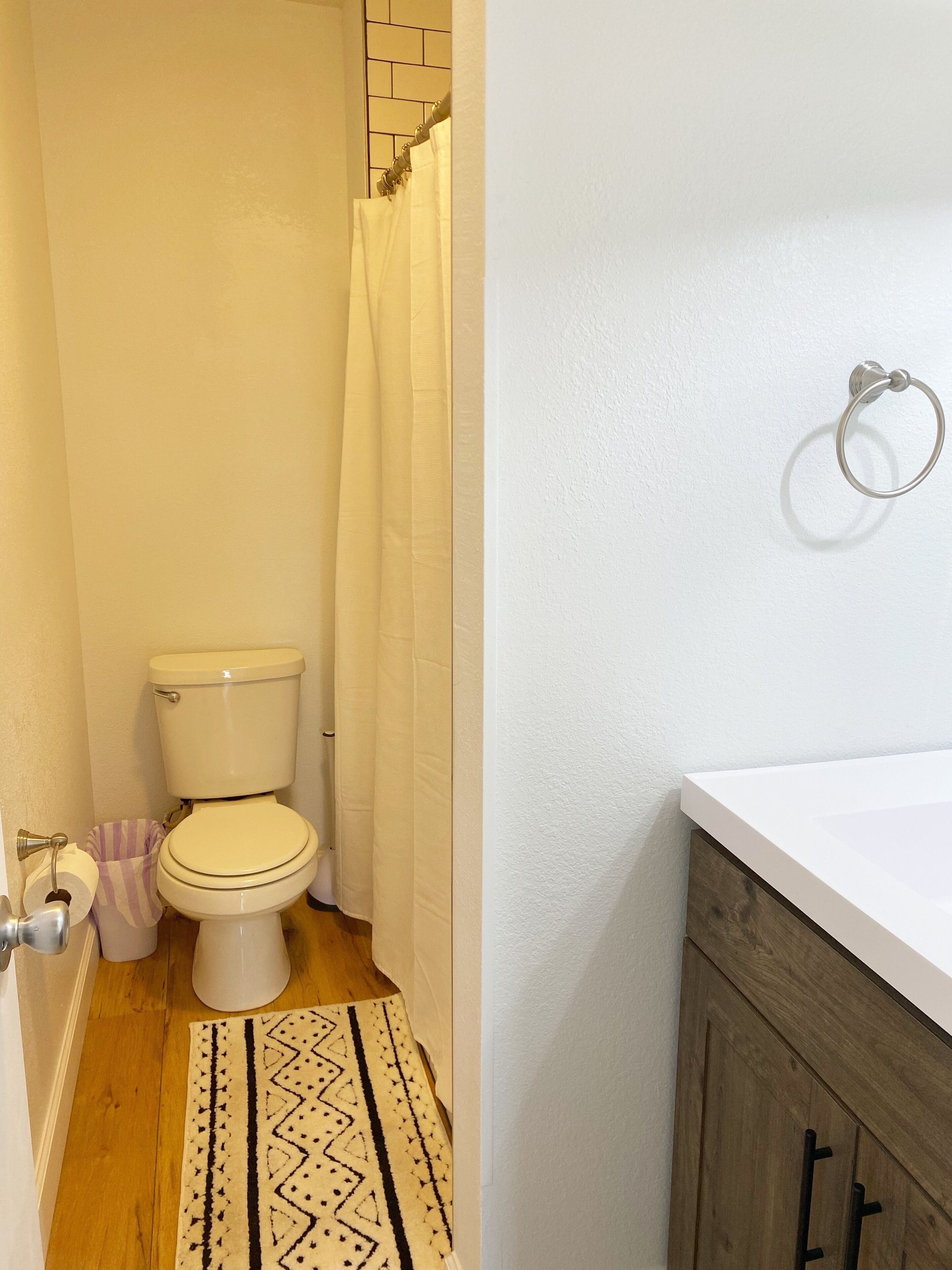 A bathroom with a toilet, a shower curtain, a towel rack, and a wooden floor.