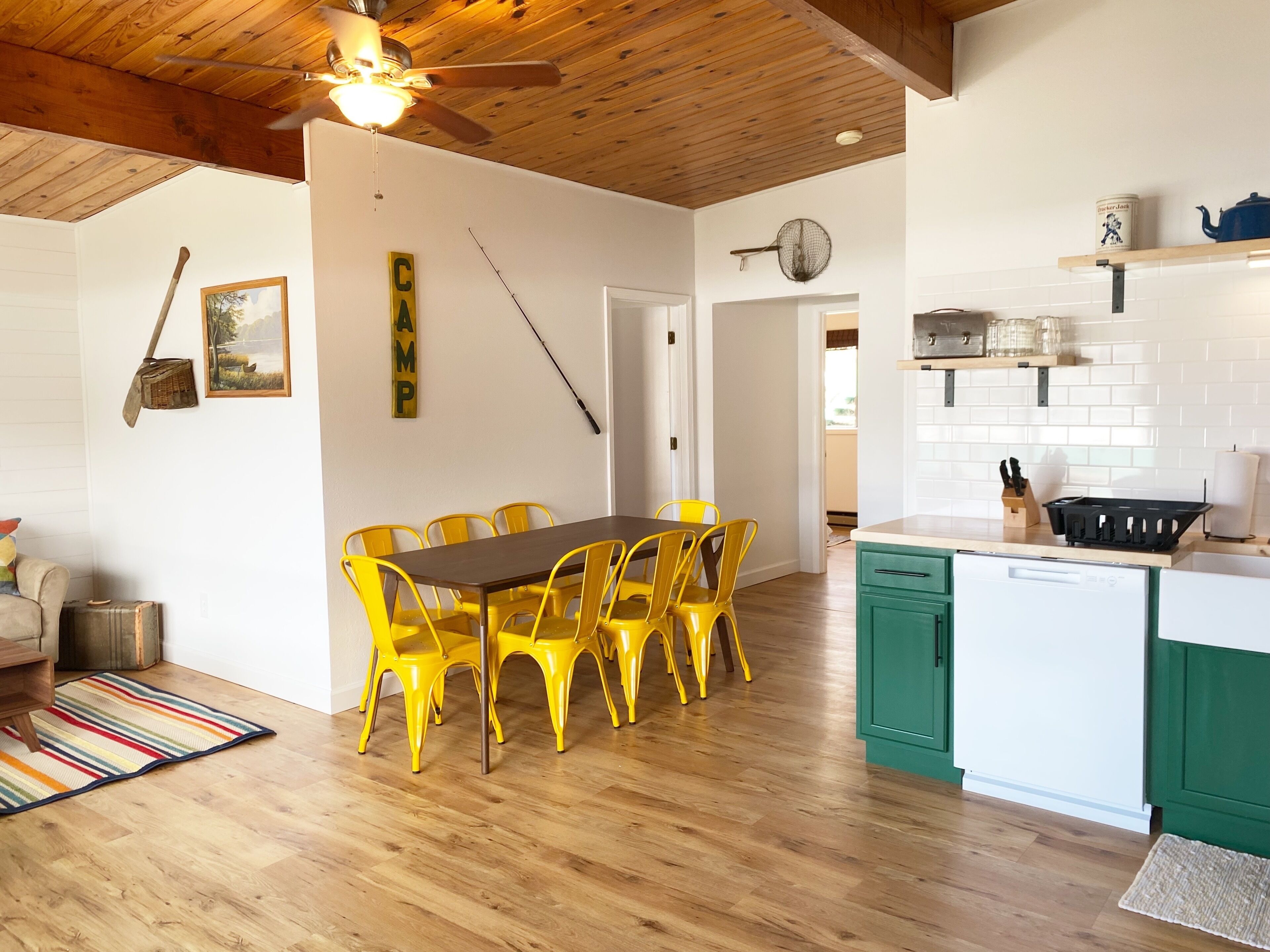 Cucina con mobili in legno, lavello e piano di lavoro. Si nota un tavolo da pranzo con sedie gialle.