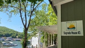 A covered outdoor area with a sign for 'Sagrada House #3' at Niuagua Hills Resort, overlooking a body of water and a dock with boats. - Niangua Hills Resort (Camdenton)
