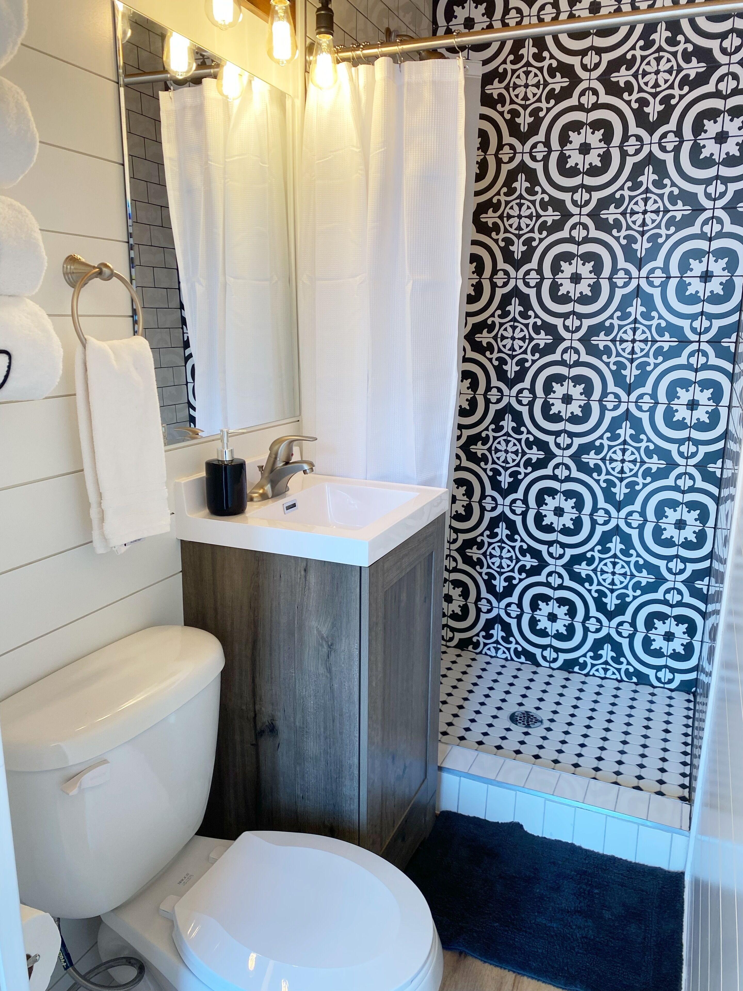 A bathroom with a white toilet, a sink with a mirror, and a shower area with patterned tiles.