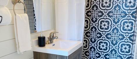 A bathroom with a white toilet, a sink with a mirror, and a shower area with patterned tiles.