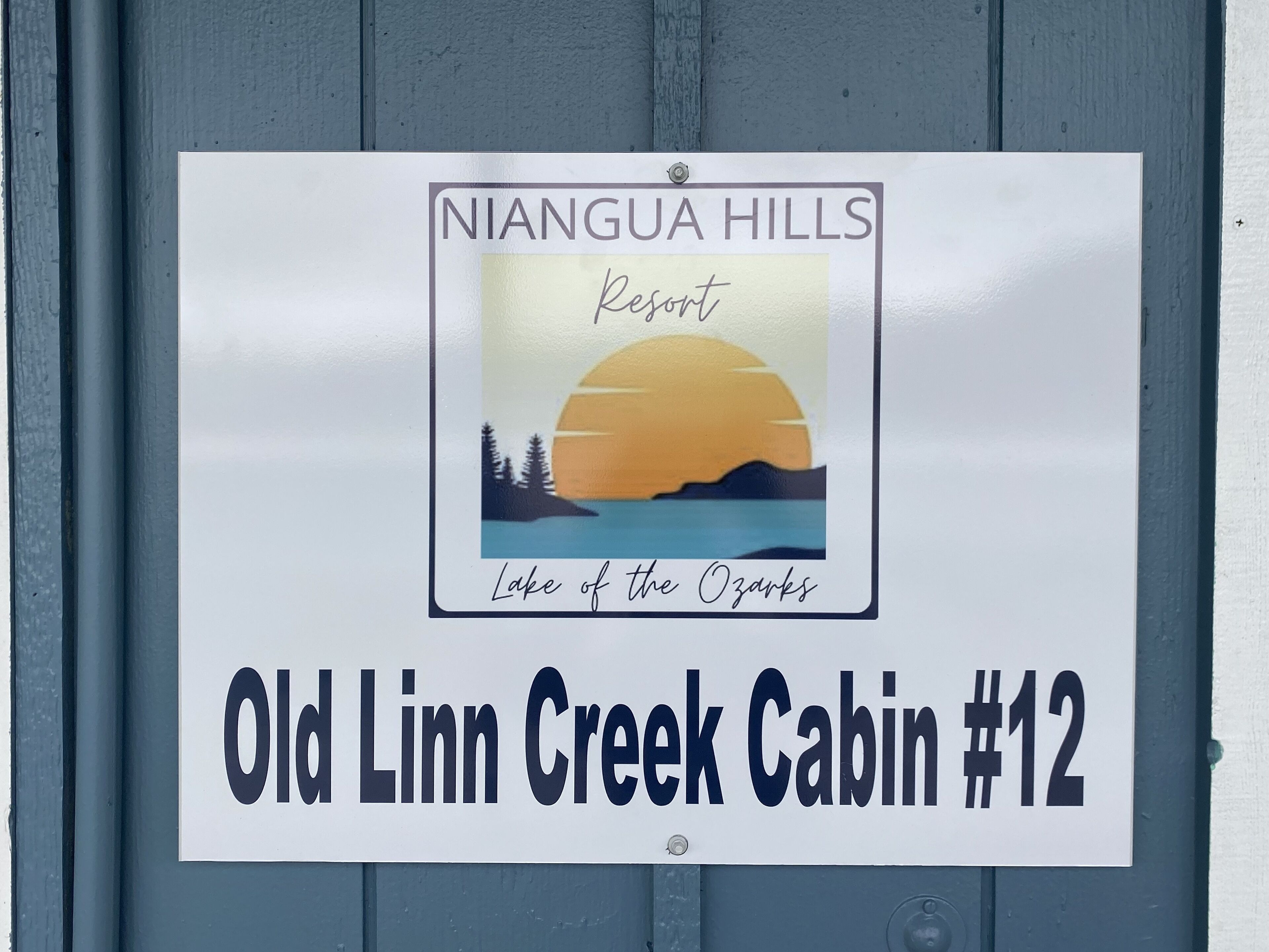 Señal para la cabaña Old Linn Creek número 12 en el Resort Niangua Hills, con una ilustración de la puesta de sol.