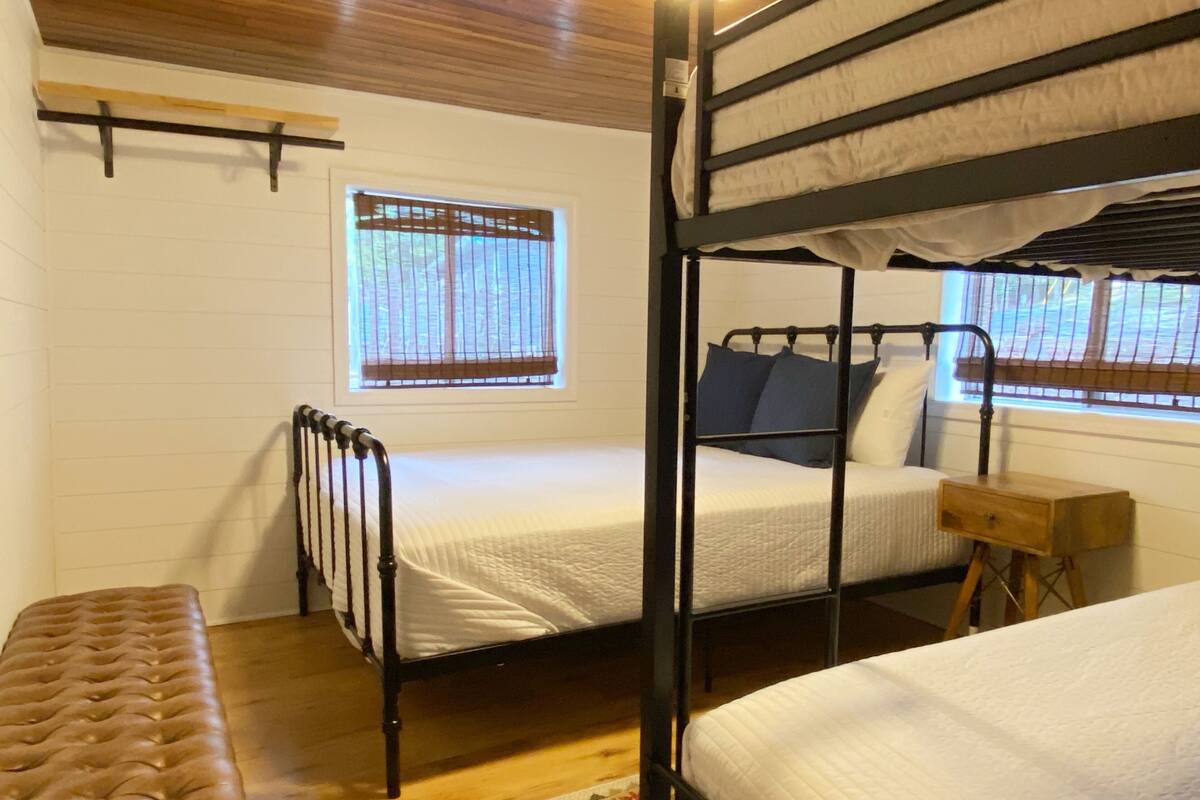 A bunk bed room with a window, a bench, and a small wooden table.