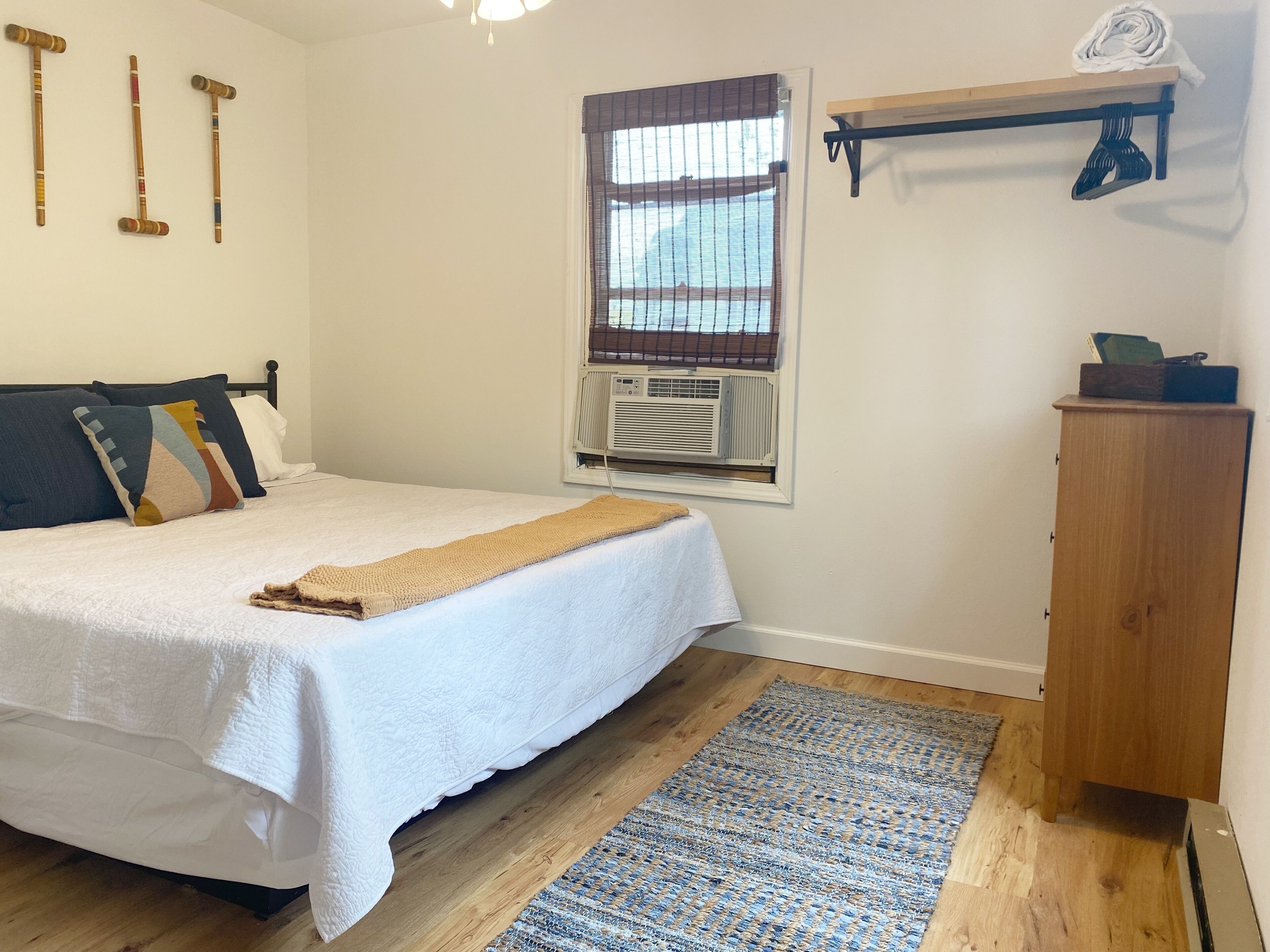 A bedroom with a bed, a wooden wardrobe, a window with blinds, and a hanging rack.