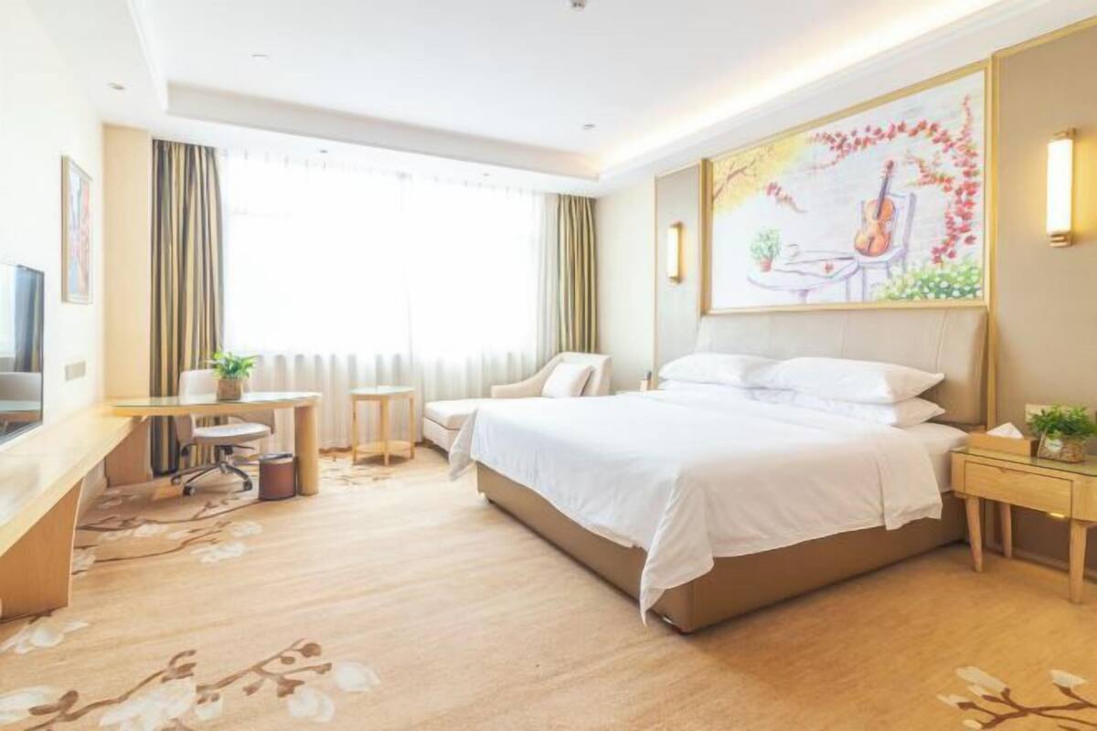 A hotel room with a large bed, a desk with a chair, a small table, and a painting on the wall.