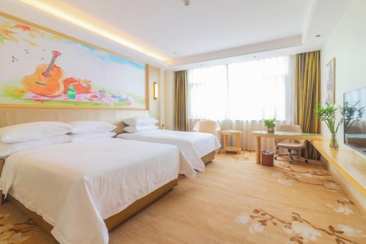 Habitación de hotel con dos camas, un escritorio, una silla, un televisor y un mural grande en la pared.