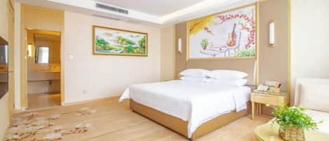 Habitación de hotel con una cama, una mesita de noche con lámpara, una pequeña mesa con planta y un cuadro en la pared.