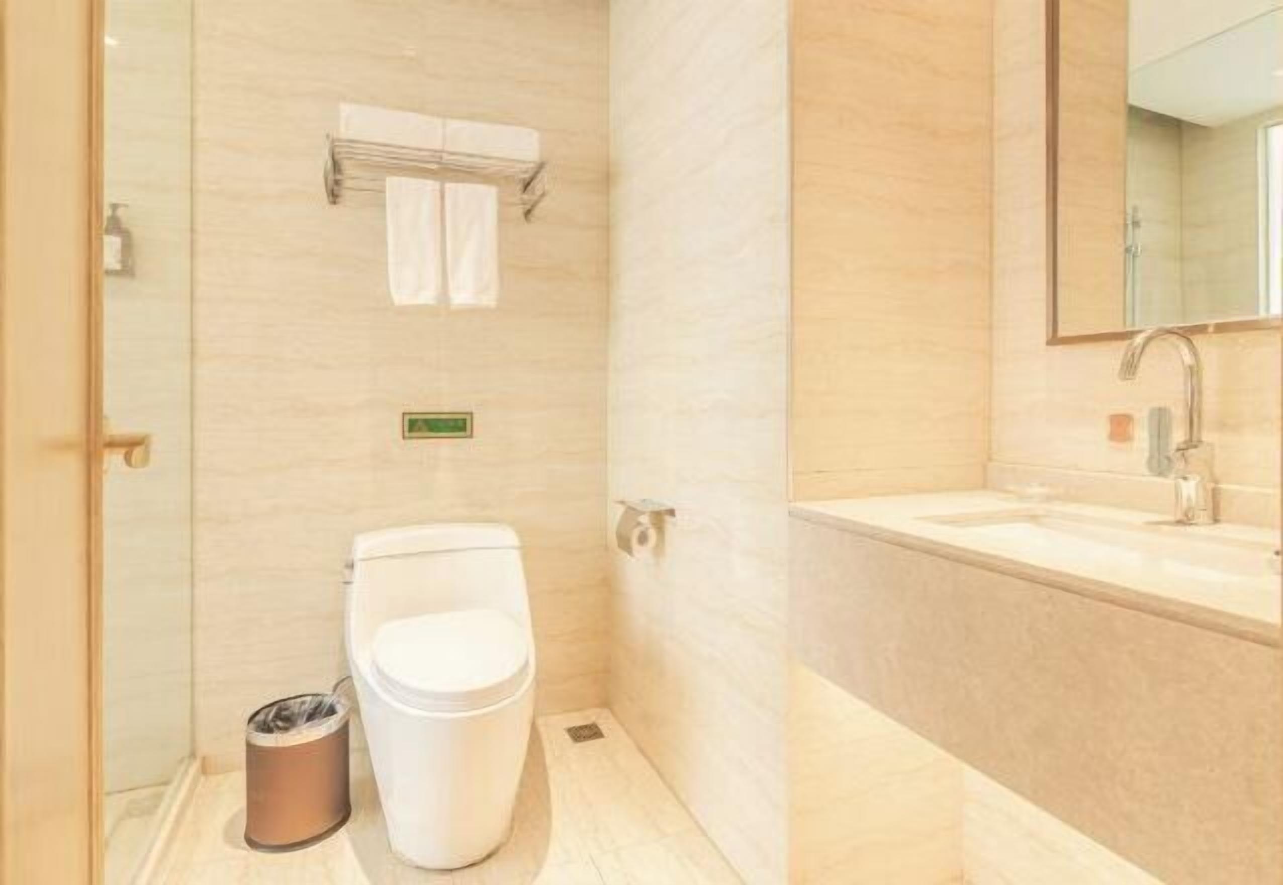 Ein Badezimmer mit Toilette, Mülleimer, Handtuchhalter und Waschbecken mit Spiegel.