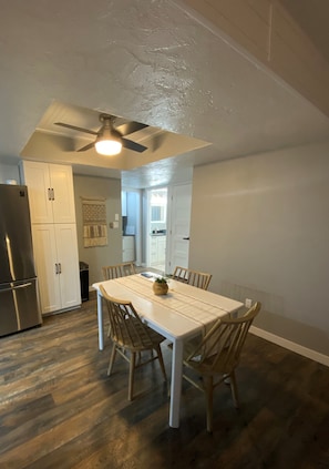 A modern kitchen with white cabinets, a stainless steel refrigerator, and a dining table with chairs.