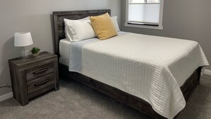 Une chambre à coucher avec un lit, une table de chevet, une lampe et une fenêtre.