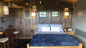 Un dormitorio rústico de madera con cama, lámparas de noche, un escritorio con sillas y cuadros en las paredes.
