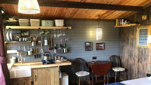 Una cocina acogedora con armarios de madera, un fregadero y una zona de comedor con mesa y sillas.