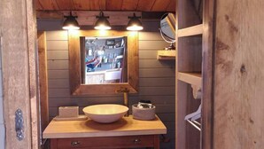 Un baño pequeño con tocador de madera, un espejo grande y tres luces fijadas a la pared.