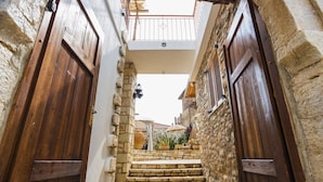 A narrow stone alleyway with wooden doors and a small set of stone steps leading to a balcony.