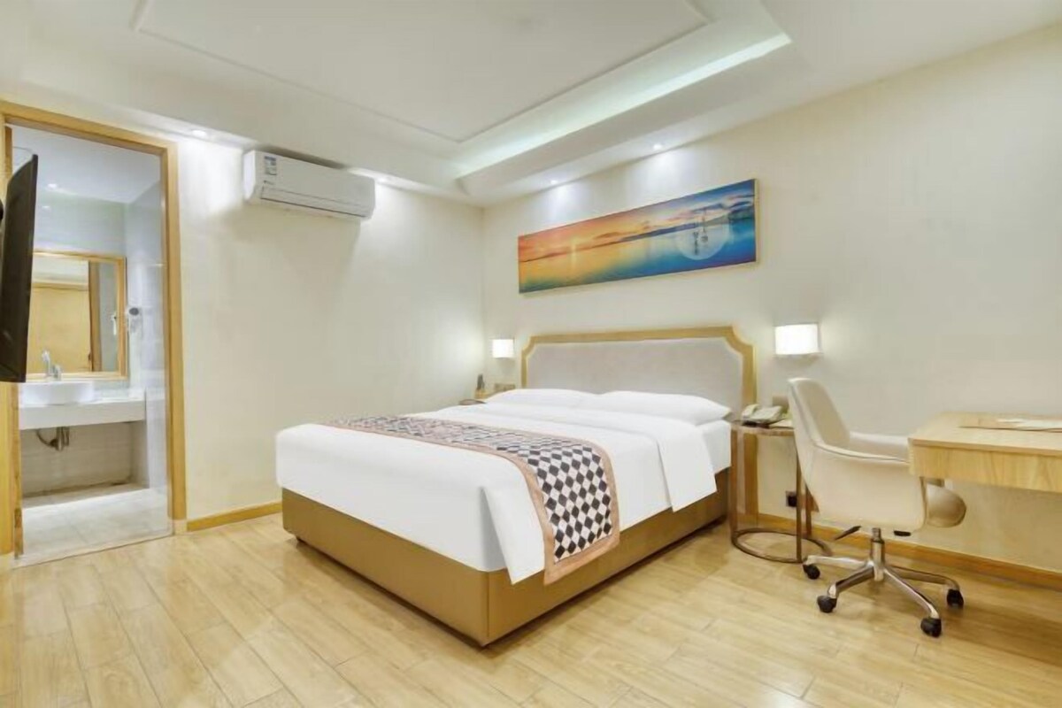 A hotel room with a bed, a desk, a chair, a mirror, and a painting on the wall.