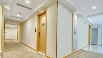 A hotel corridor with wooden doors, a carpeted floor, and a white wall with a green sign.