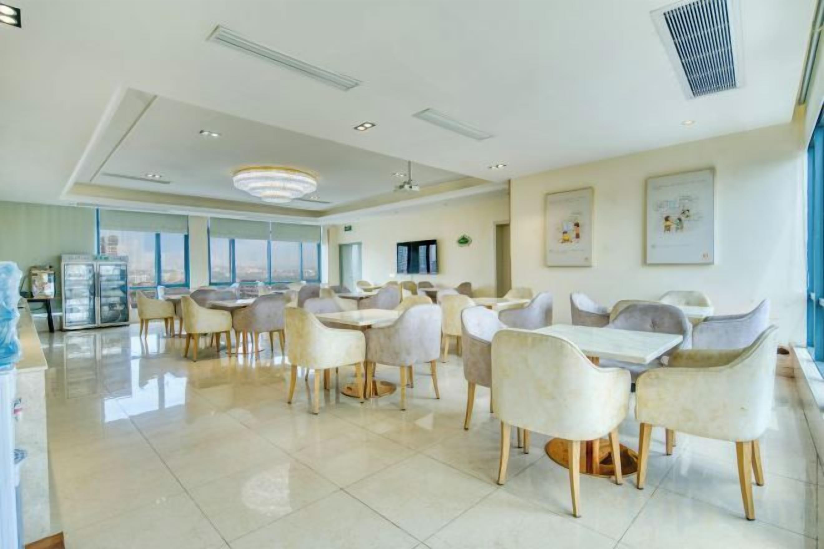 Uma sala de jantar ampla com várias mesas e cadeiras, janelas grandes e um lustre moderno.