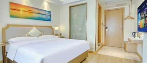 A hotel room with a large bed, a painting on the wall, a door, and a small table with a kettle.