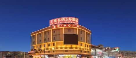 Un hôtel à plusieurs étages, doté d’une façade incurvée, d’une enseigne lumineuse et dont l’image se reflète dans l’eau devant l’établissement.