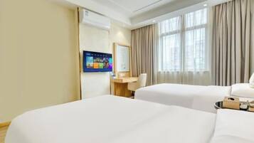 A hotel room with two beds, a desk, a TV, and large windows with curtains.