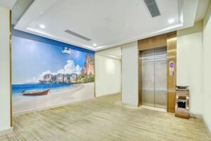 A hotel lobby with a mural of a beach scene, an elevator, and a reception desk. - Vienna 3 Best Hotel (Foshan Jinsha Central Square) (Foshan)