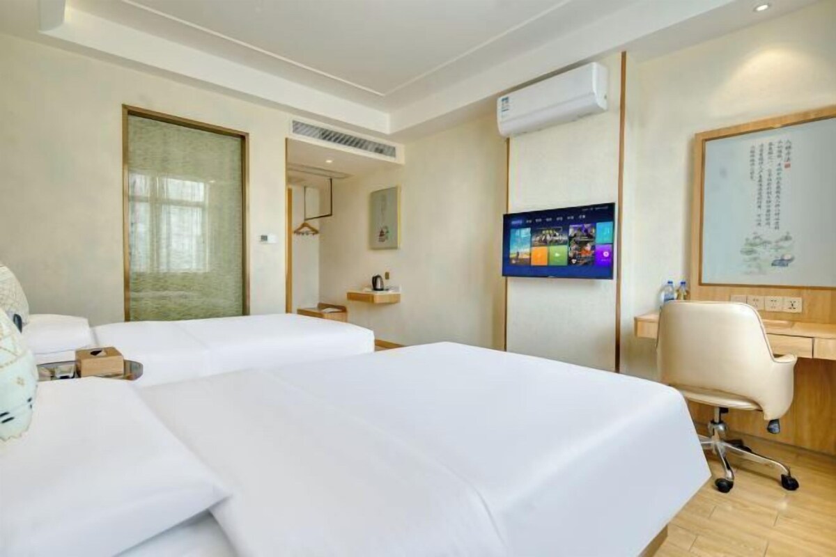 A hotel room with two beds, a desk with a chair, a television, and a whiteboard.