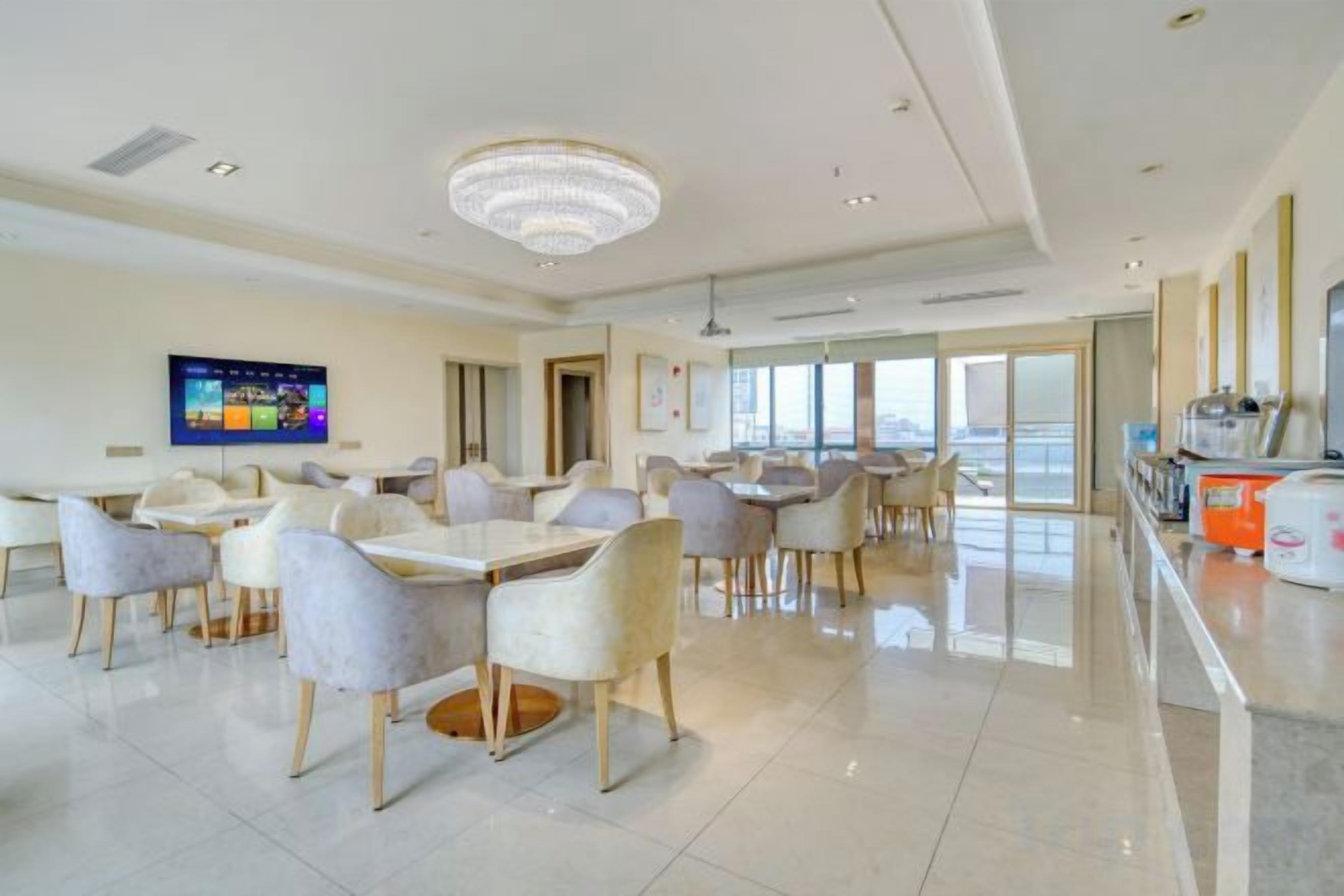 A spacious dining area with multiple tables and chairs, a television screen, and a large chandelier.