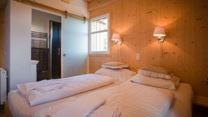 Une chambre avec deux lits, des murs en bois, une fenêtre avec des stores et des lampes fixées au mur.