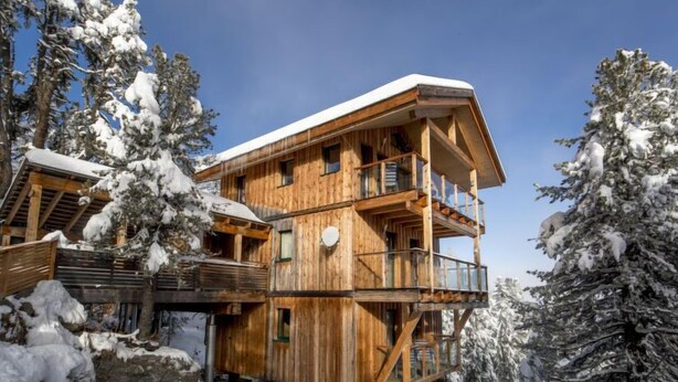 Une cabane en bois dotée d’un balcon, entourée d’arbres couverts de neige.