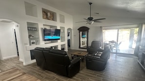 Ein modernes Wohnzimmer mit Flachbildfernseher, Ledersofas, einem Holztisch und Deckenventilator.