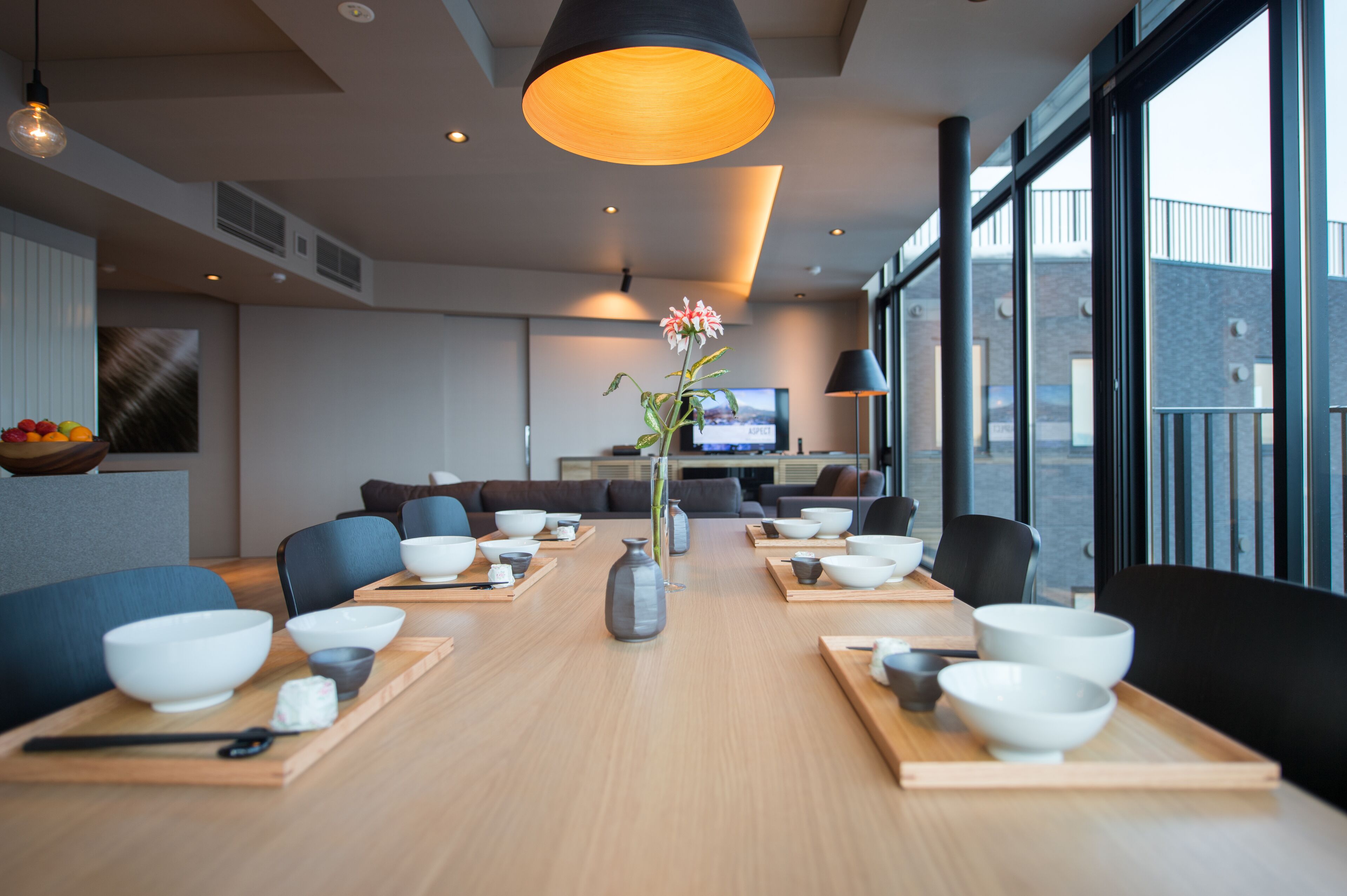 A modern dining area with a long table set for a meal, surrounded by comfortable seating.