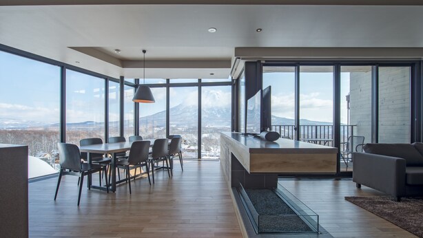 A modern living room with a large dining table, comfortable seating, a TV, and a view of a mountain. - Aspect Luxury Apartments by H2 Life (Kutchan)