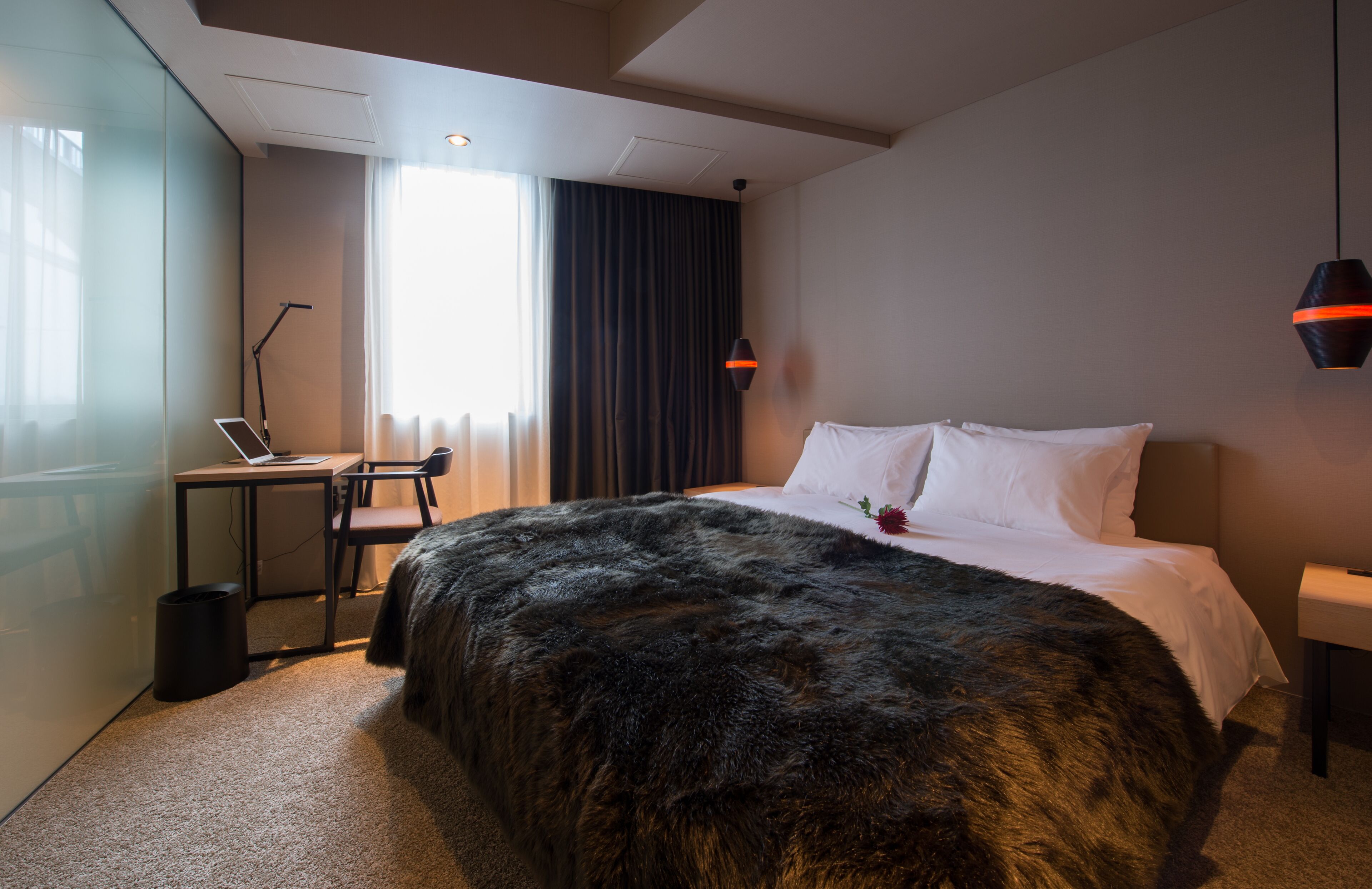 A hotel room with a large bed, a desk with a laptop, a chair, and a small trash bin.