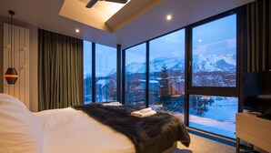A modern bedroom with a large bed, a TV, and a view of a snowy mountain landscape. - Aspect Luxury Apartments by H2 Life (Kutchan)