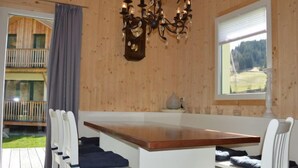 A cozy cabin interior with a wooden interior, a chandelier, a large window with a view, and a balcony.