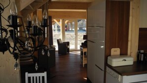 A compact kitchen with a refrigerator, a small dining area with a white chair, and a wooden ceiling.