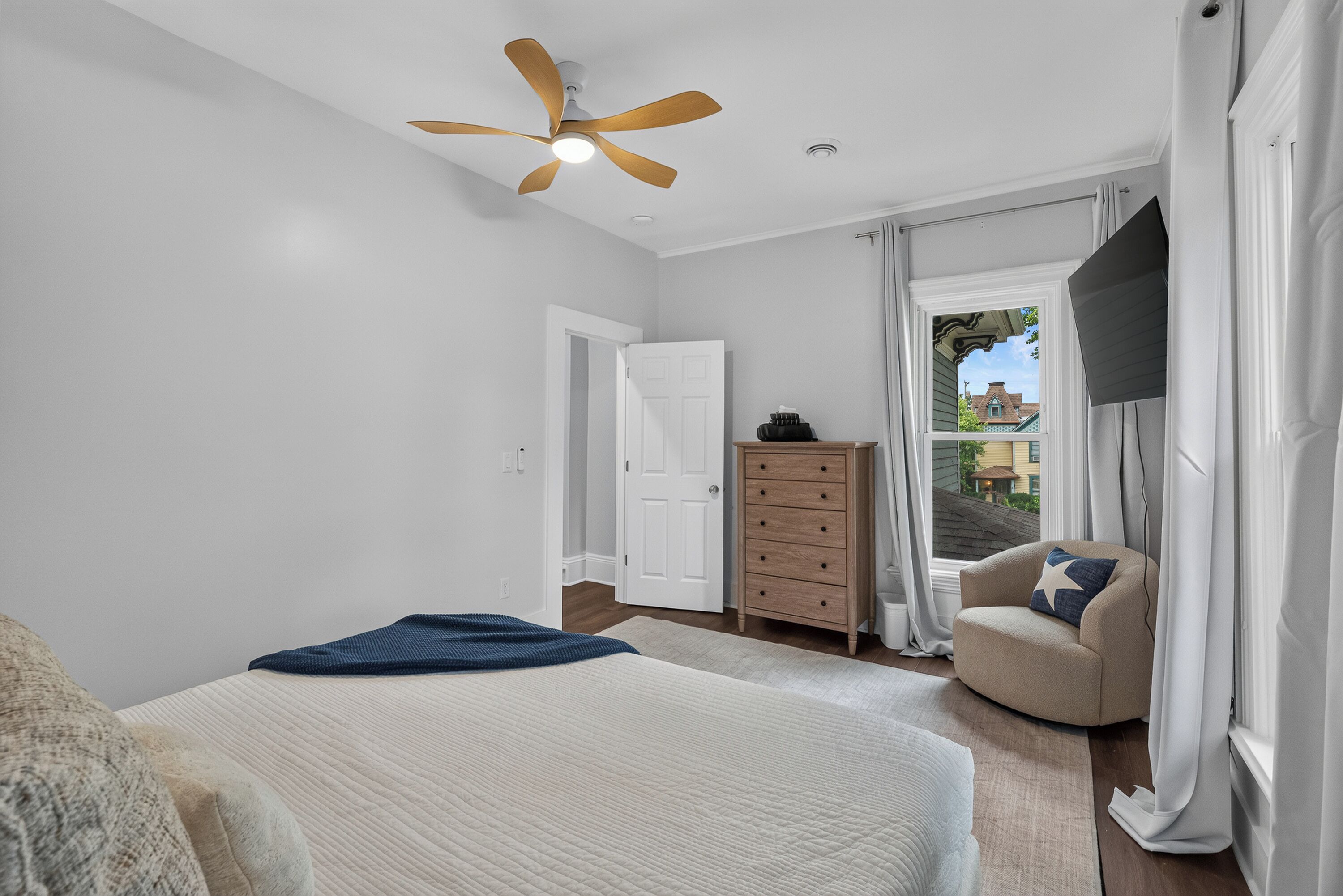 A bedroom with a bed, a dresser, a chair, a ceiling fan, and a window with curtains.