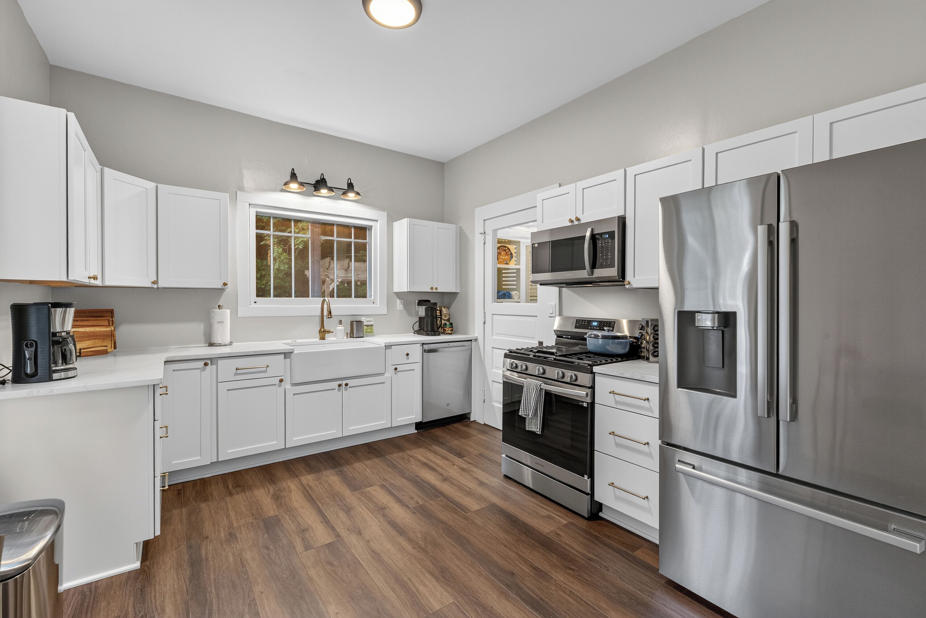 A modern kitchen with white cabinetry, stainless steel appliances, and a window overlooking a garden.