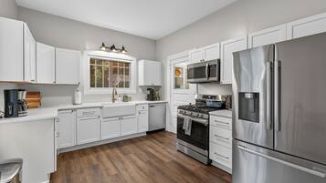 A modern kitchen with white cabinetry, stainless steel appliances, and a window overlooking a garden.