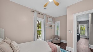 A bedroom with a bed, a chair, a window, and a door leading to another room. - Victorian · Game Room · Walk to Beach + Downtown (Lake Geneva)