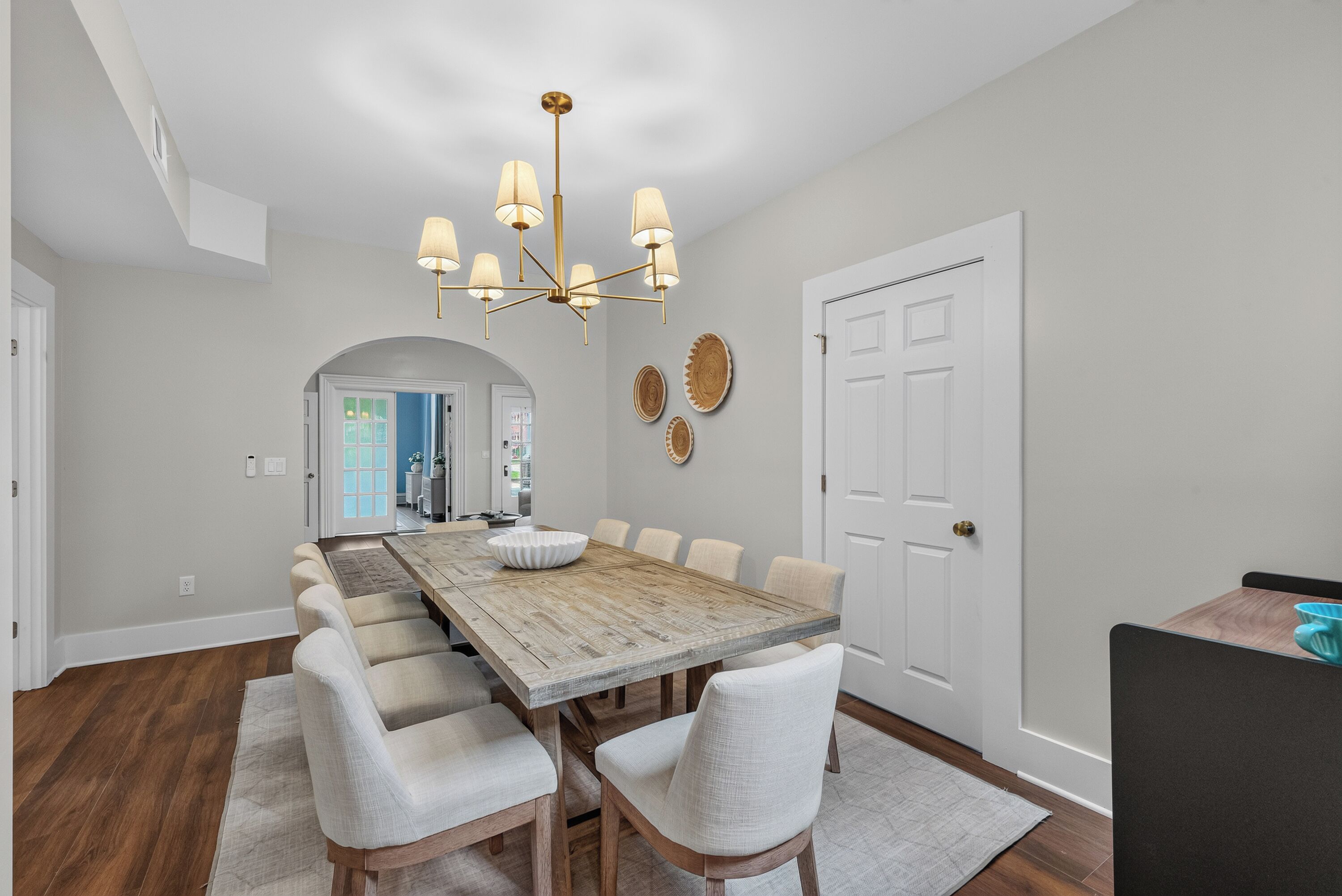 A dining room with a long wooden table, six chairs, and a chandelier.
